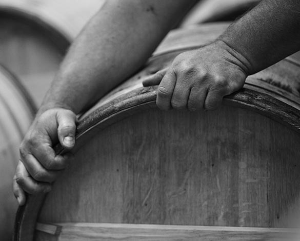 A macroshot in black and white of a vineyard workers hands on the side of a barrel, turning it